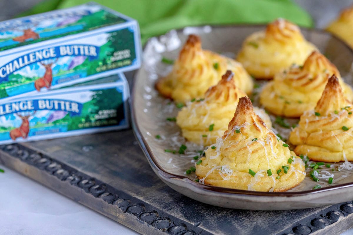 six duchess potatoes sitting on a brown serving tray with boxes of Challenge butter to the left of the tray.