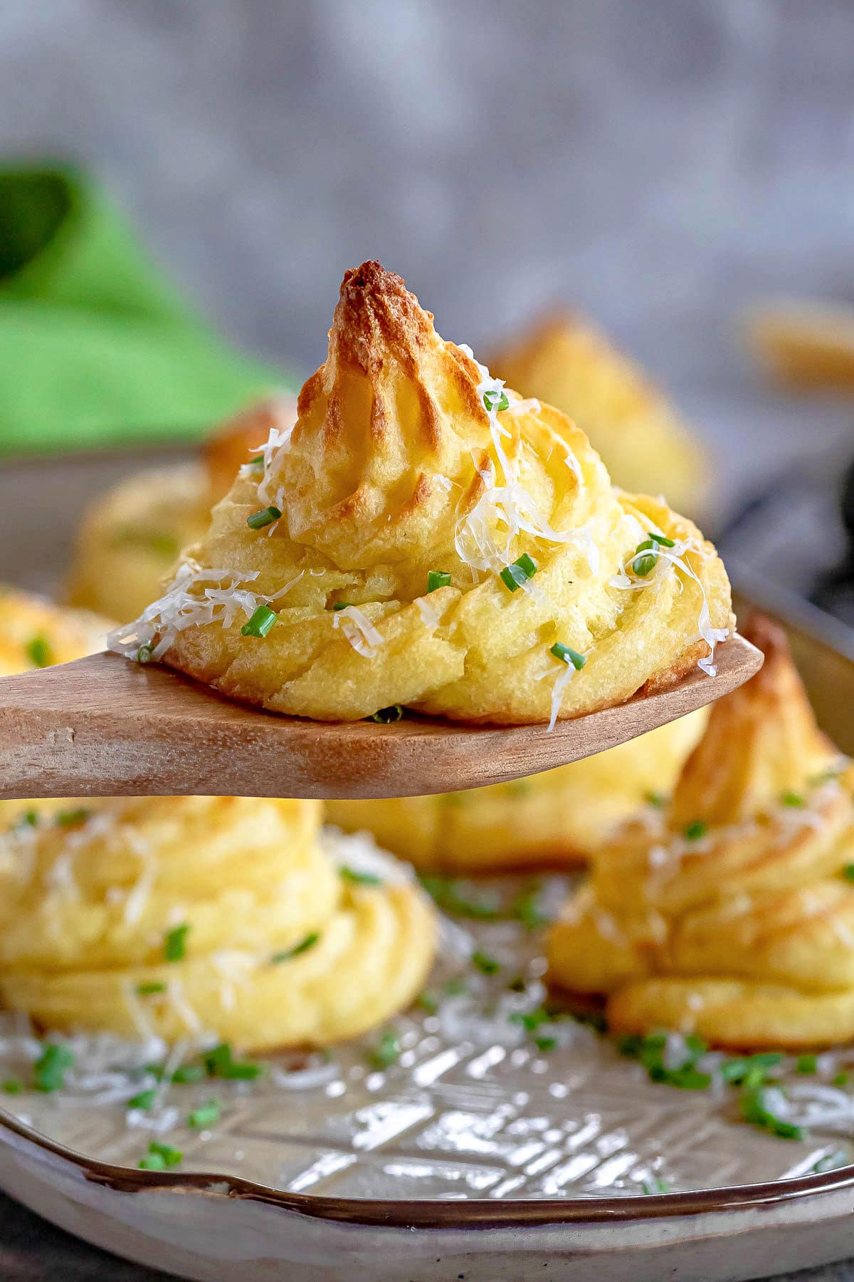 single Duchess potato held up above a tray with a wooden server. granished with chives and Parmesan.