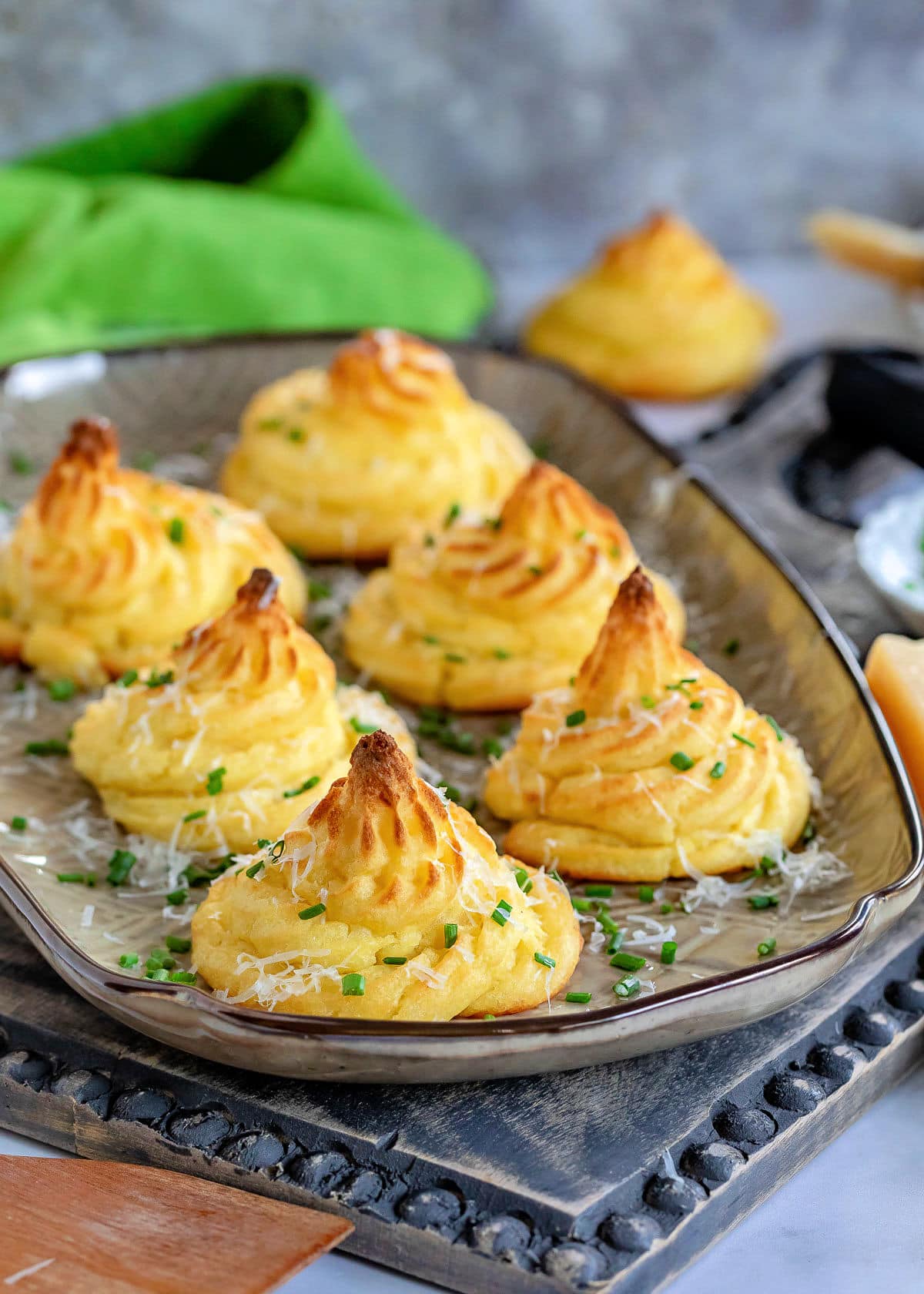 large brown tray with six duchess potatoes garnished with Parmesan cheese and snipped chives.