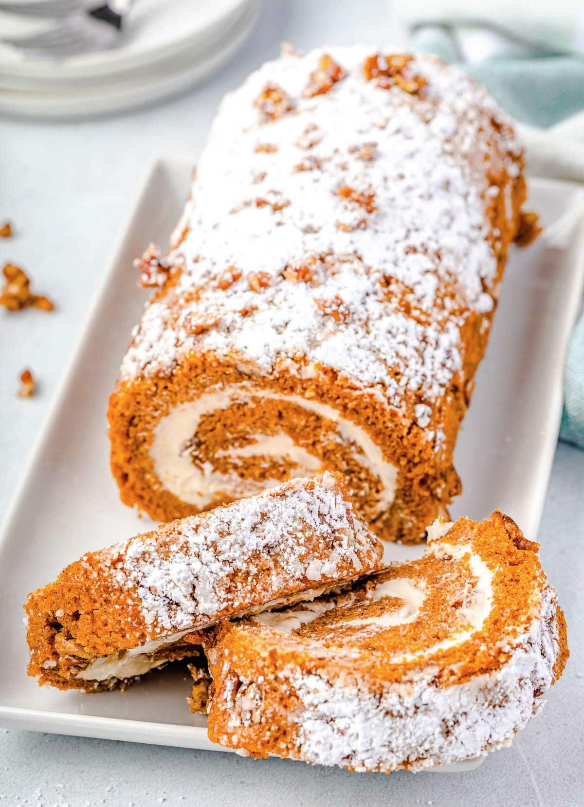 pumpkin roll with two slices cut off sitting on white rectangle serving plate.