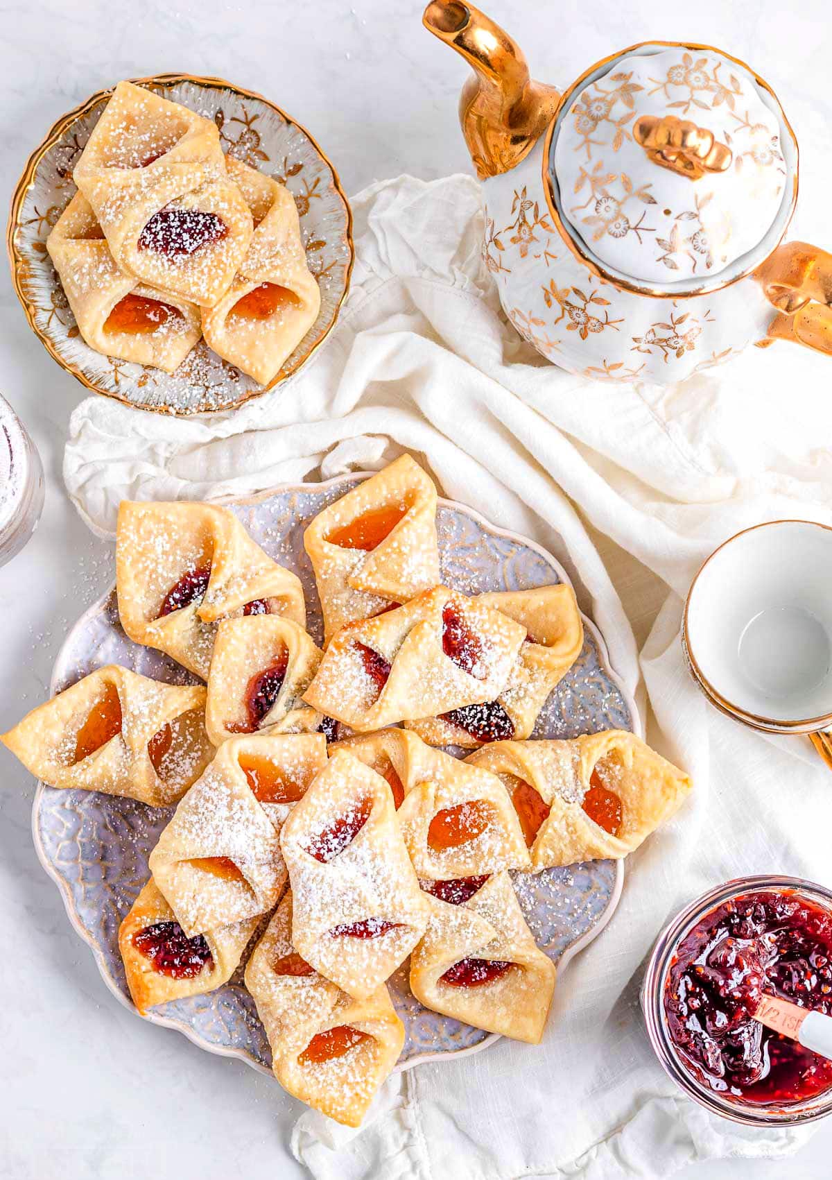 a plate of kolacky cookies with a smaller plate off to the side. this is a top down flat lay view of the cookies. small jar of jam in lower right corner.