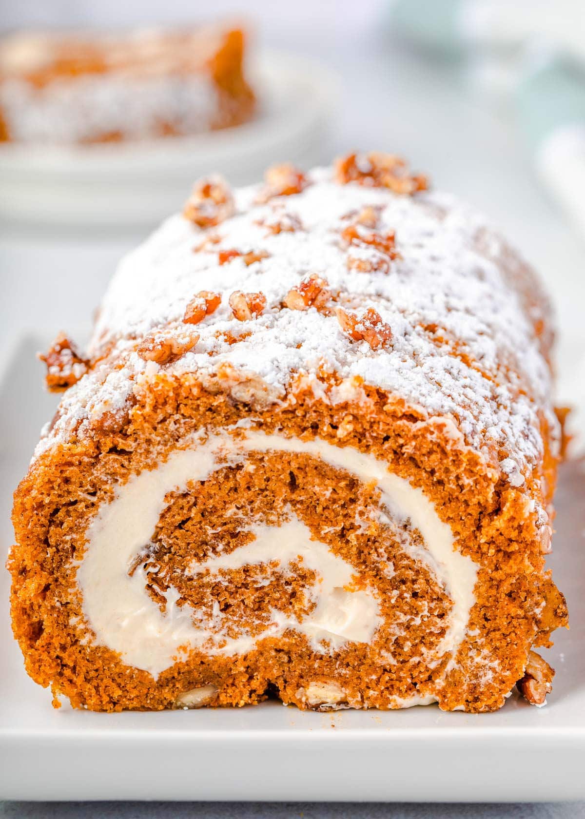 pumpkin roll with candied pecans sitting on long white tray dusted with powdered sugar. 
