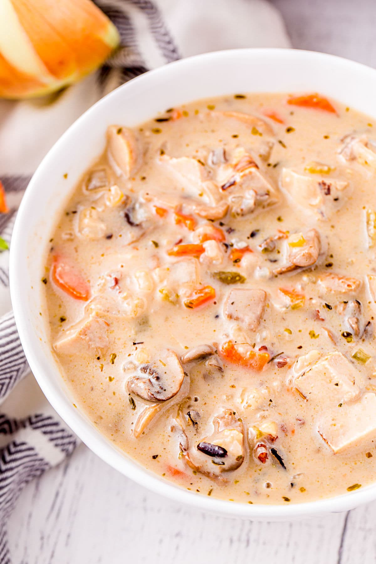 close up look at turkey soup with wild rice and mushrooms in a white soup bowl.