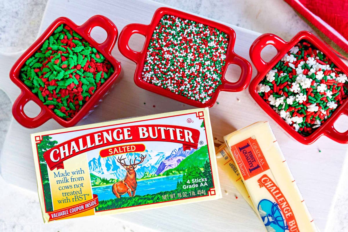 top down shot showing a box of butter and various christmas sprinkles separated into small red ceramic bowls.