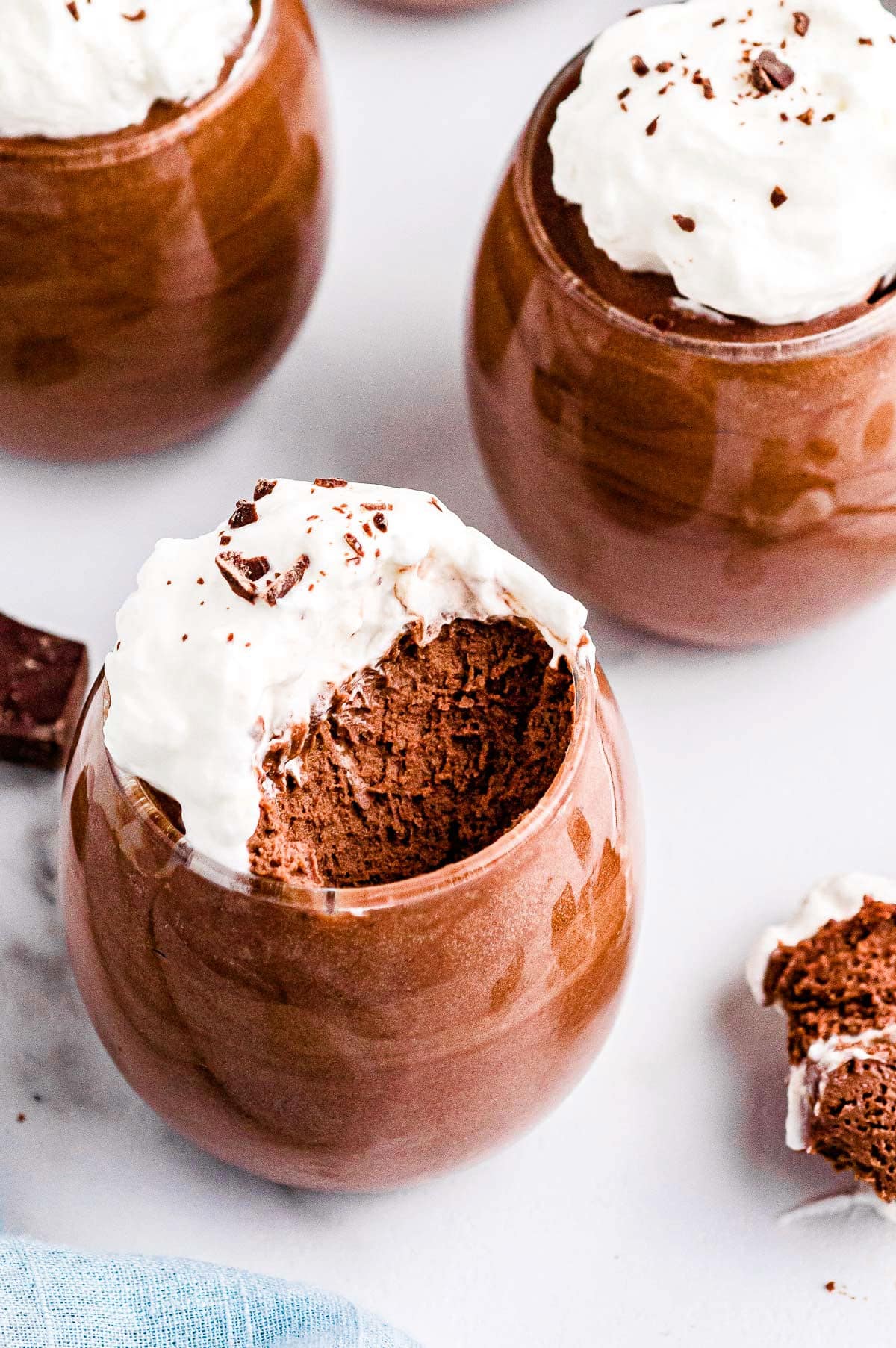 chocolate mousse in a wine glass with a bite taken showing the airy texture of the mousse. Two more glasses in background.