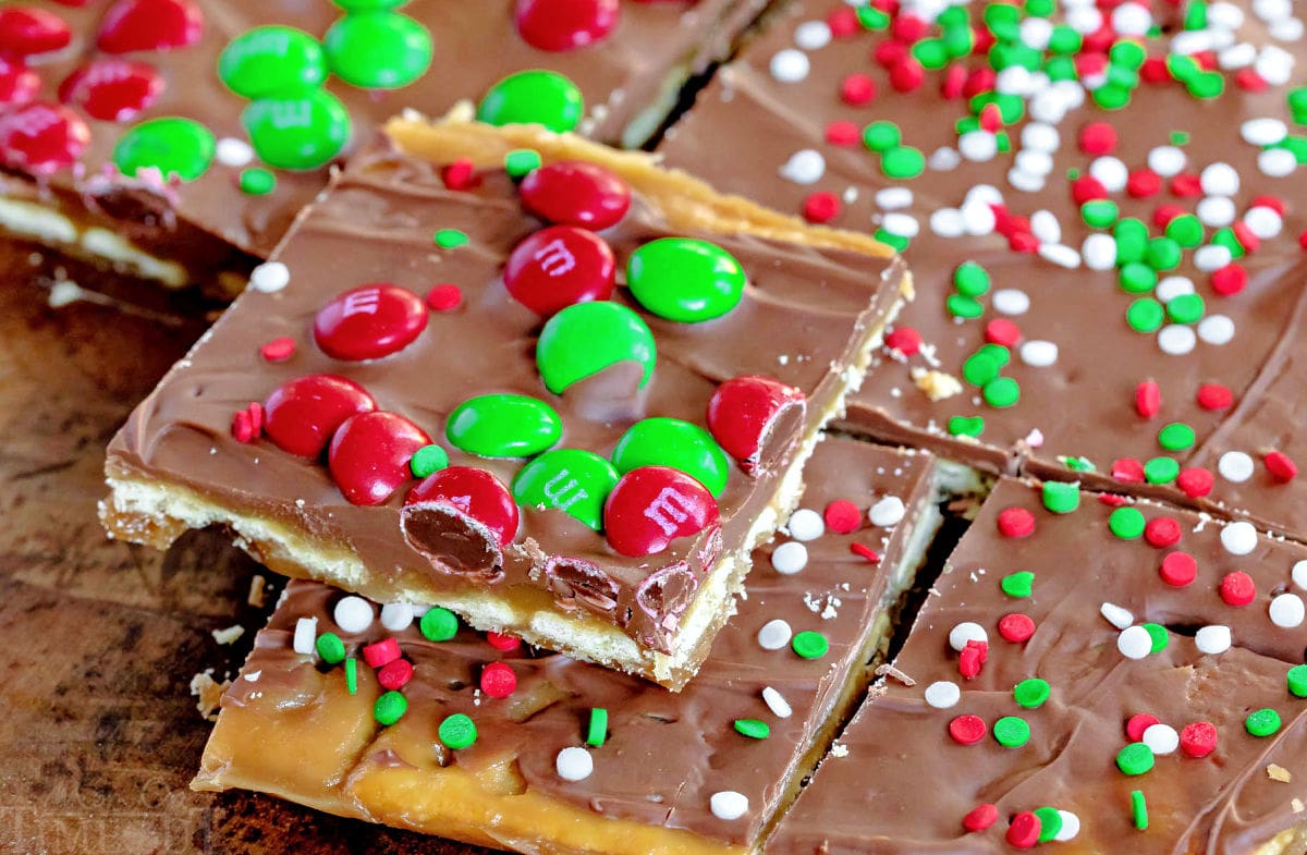 piece of christmas crack topped with m&ms sitting on more saltine cracker toffee that needs to be cut into pieces.