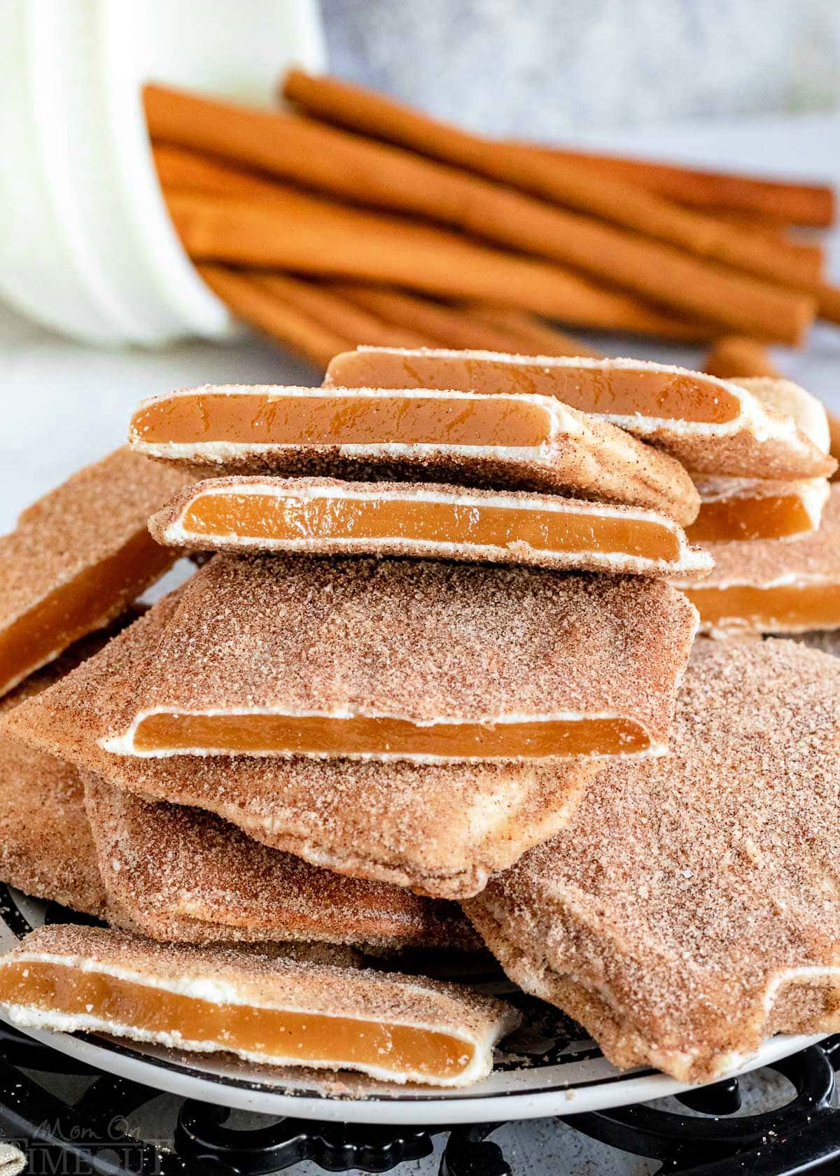 pile of churro toffee on a black and white plate with cinnamon sticks in the background.