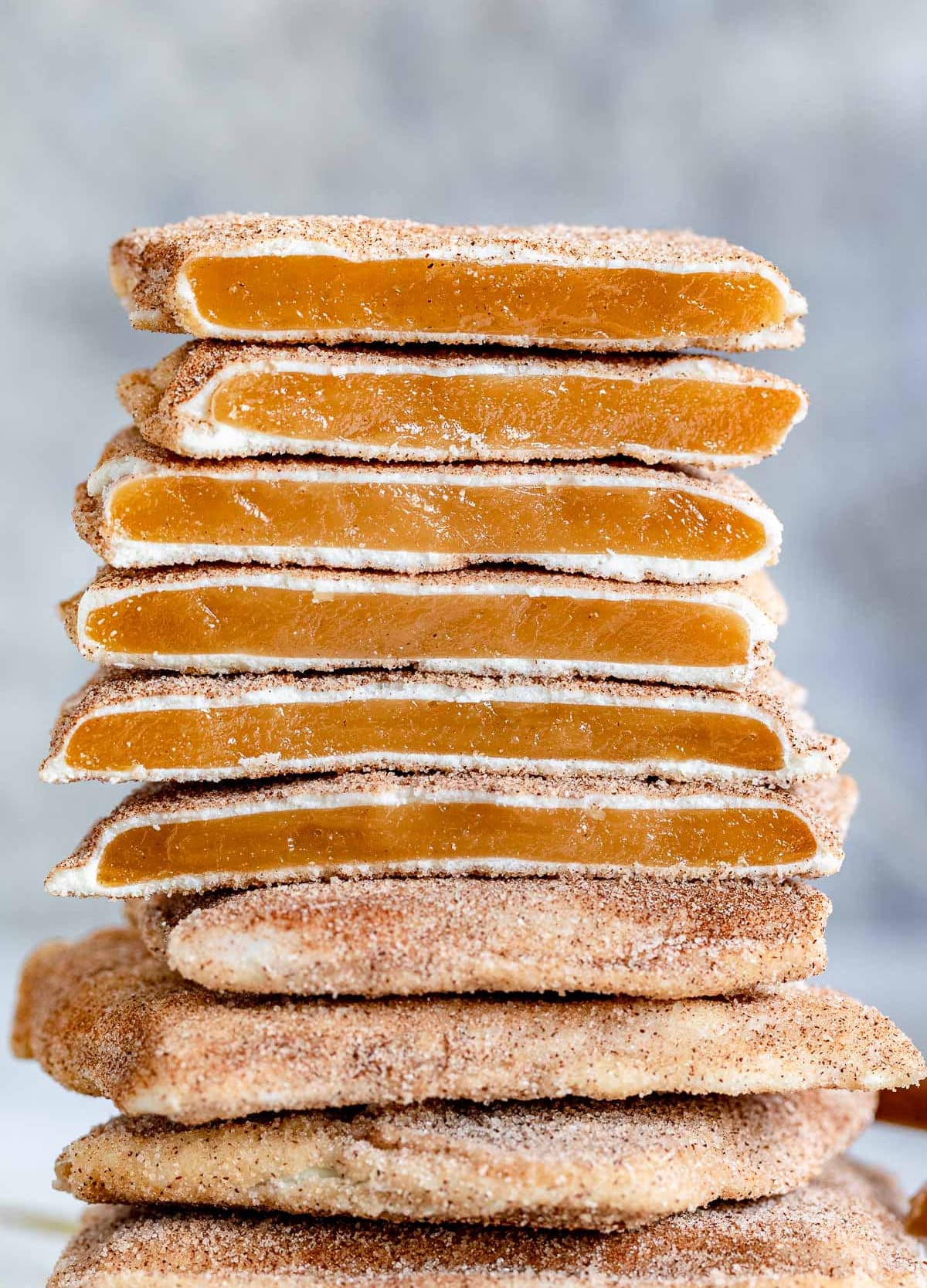 square churro toffee stacked on one another with several pieces broken in half so you see the toffee, the white chocolate layer and cinnamon sugar coating. 