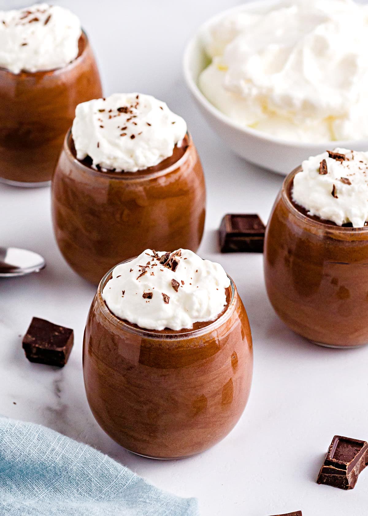 four glasses with chocolate mousse in them topped with whipped cream and chocolate shavings ready to be eaten.