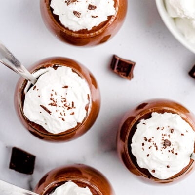 top down view of four glasses with chocolate mousse in them topped with whipped cream and chocolate shavings ready to be eaten.