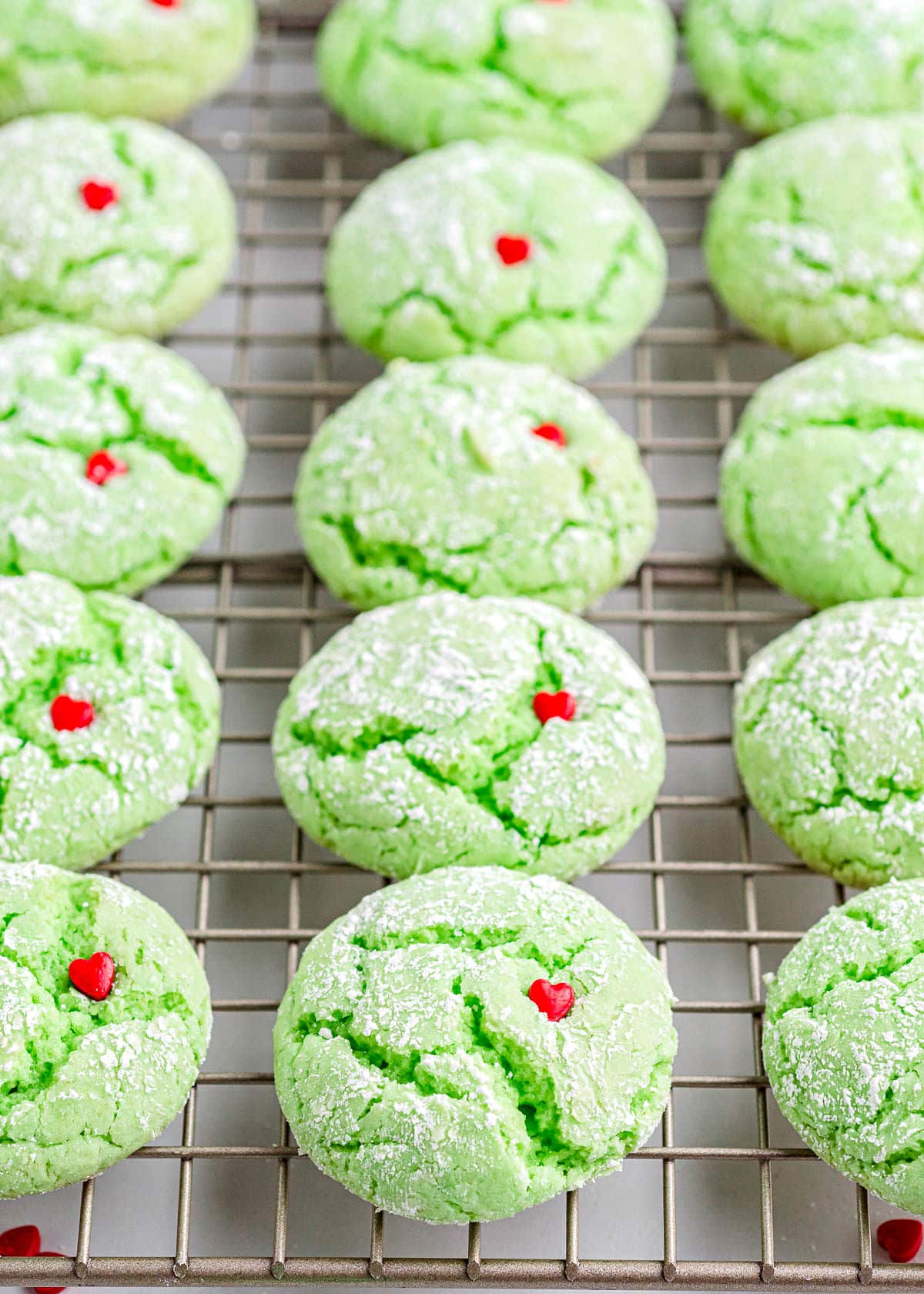 grinch cookies lined up in a row on a cooling rack with red heart sprinkles pressed into the top.
