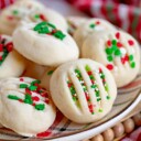 whipped shortbread cookies on a Christmas plate with red, green and white sprinkles. Plate is on cutting board sitting next to a Christmas towel.