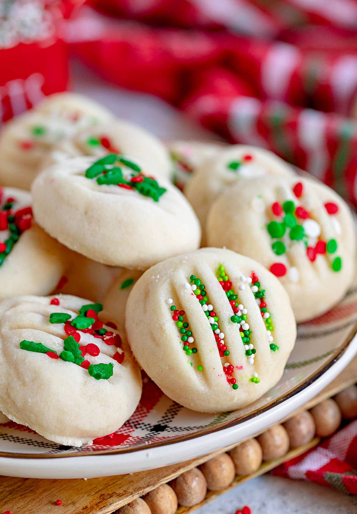 whipped shortbread cookies on a Christmas plate with red, green and white sprinkles. Plate is on cutting board sitting next to a Christmas towel.