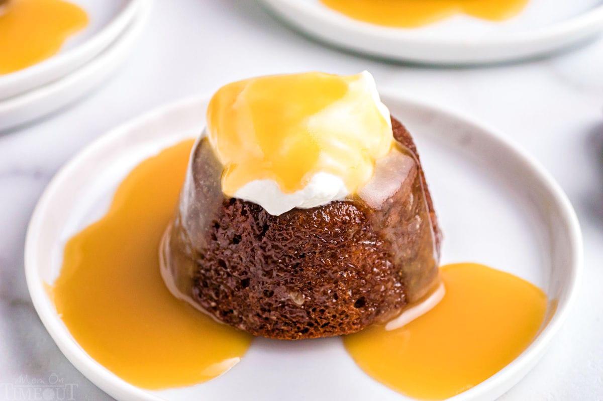 angled look at one sticky toffee pudding topped with whipped cream and more toffee sauce on a single white dessert plate.