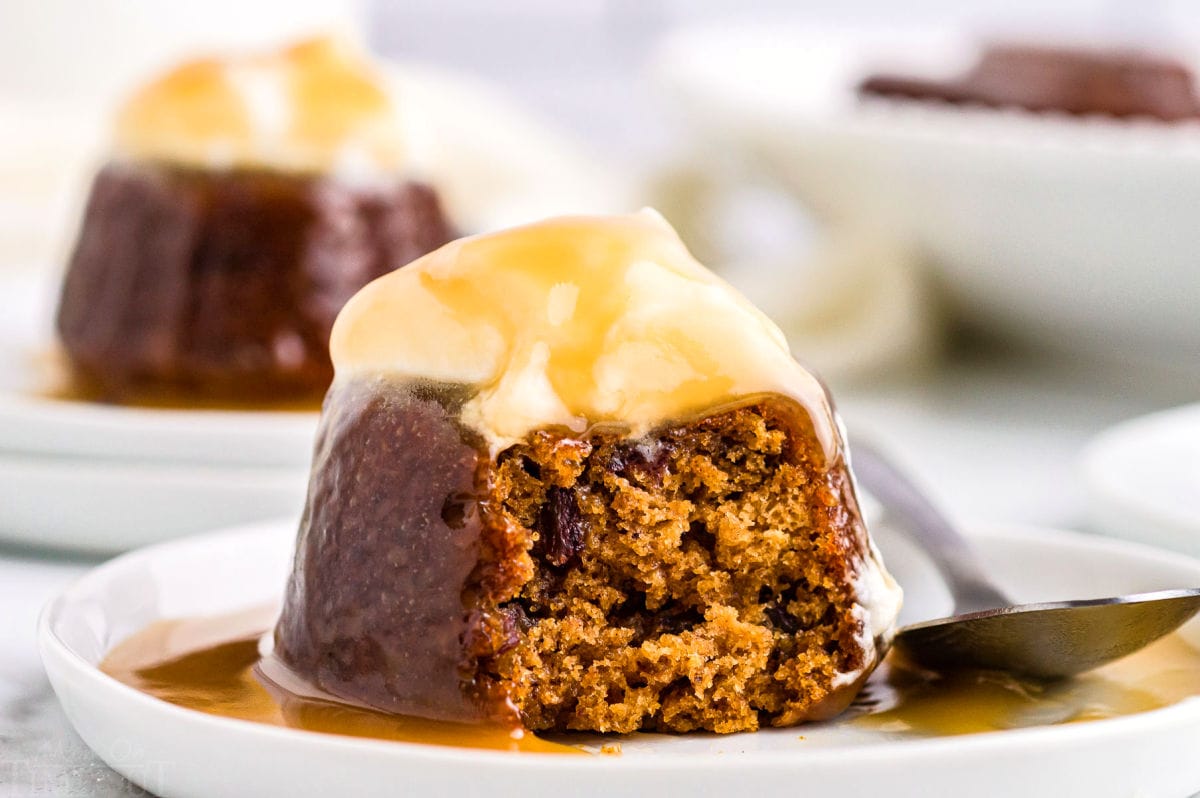 sticky toffee pudding on white dessert plate topped with whipped cream and toffee sauce.