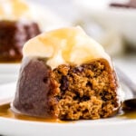 sticky toffee pudding on white dessert plate topped with whipped cream and toffee sauce.