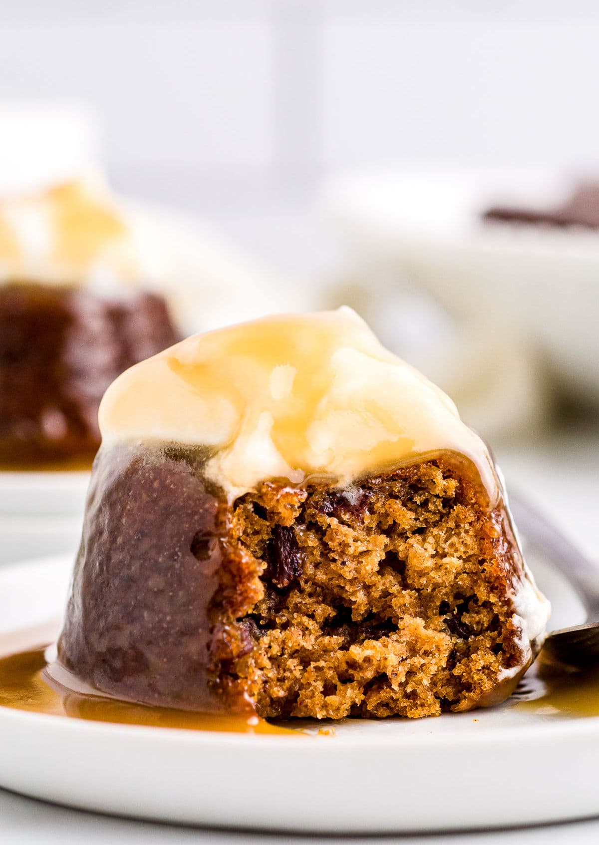 sticky toffee pudding on white dessert plate topped with whipped cream and toffee sauce.