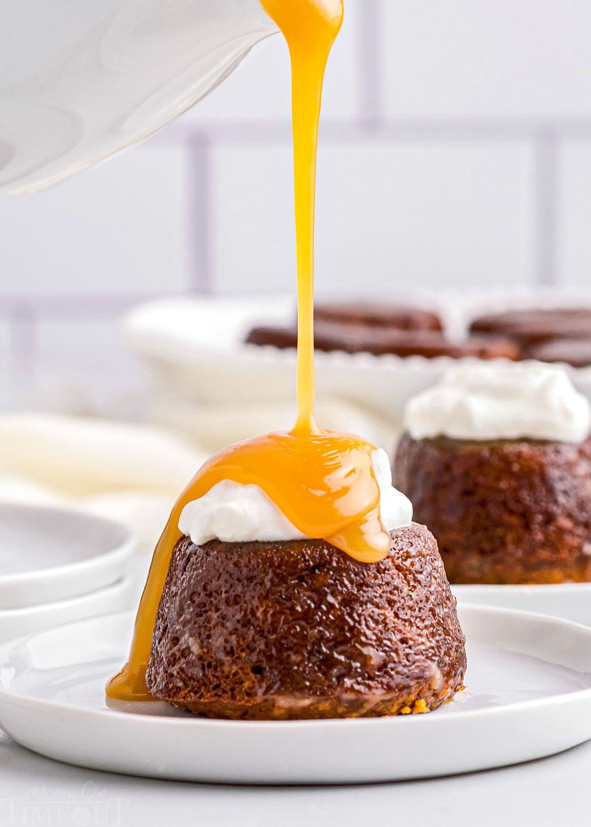 toffee sauce being poured over sticky toffee pudding on white plate.