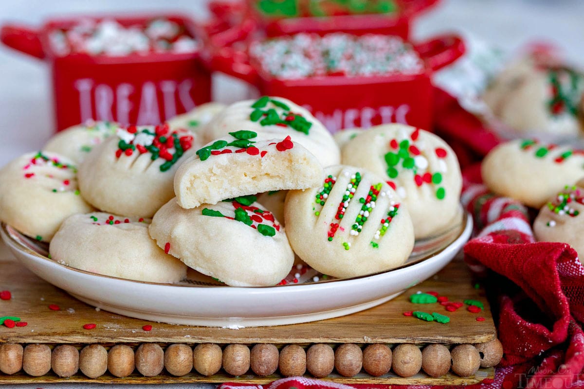 a plate of Christmas cookies with the top cookie half eaten. small red jars of sprinkles can be seen in the background.