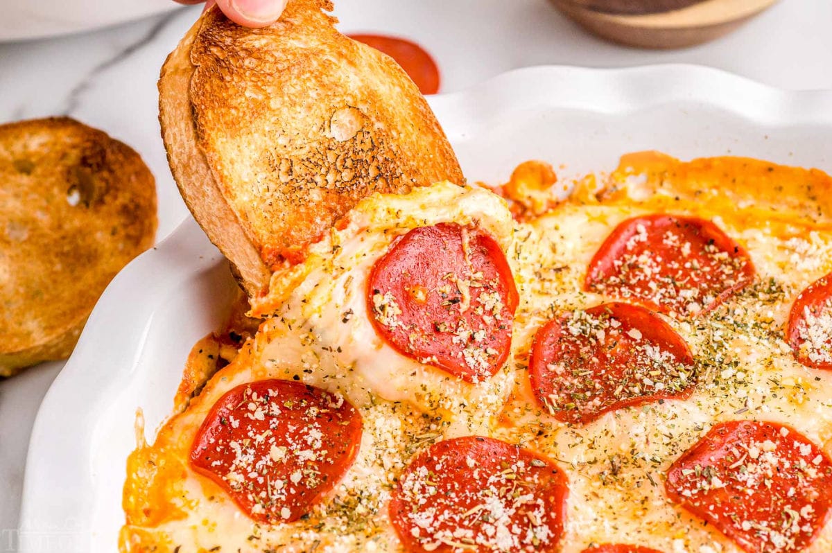 garlic bread being dipped into hot pizza dip topped with pepperonis.