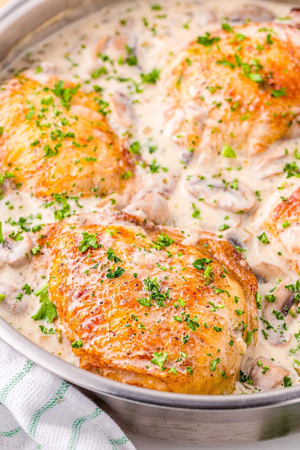 skillet with four chicken thighs browned and simmering in a white wine mushroom sauce. A sprinkling of parsley over the top provides a nice contrast.