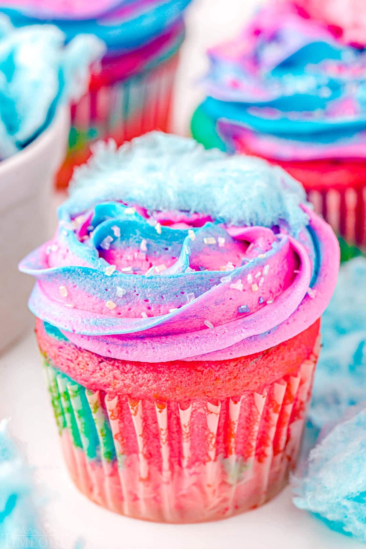 close up look at a swirled cupcake with swirled frosting made with blue and pink frosting. Small bit of cotton candy on top of the cupcake.
