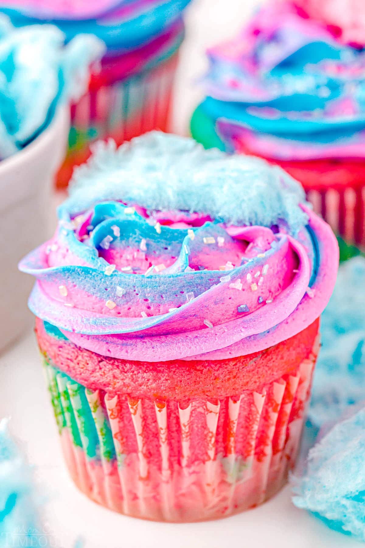 close up look at a swirled cupcake with swirled frosting made with blue and pink frosting. Small bit of cotton candy on top of the cupcake.