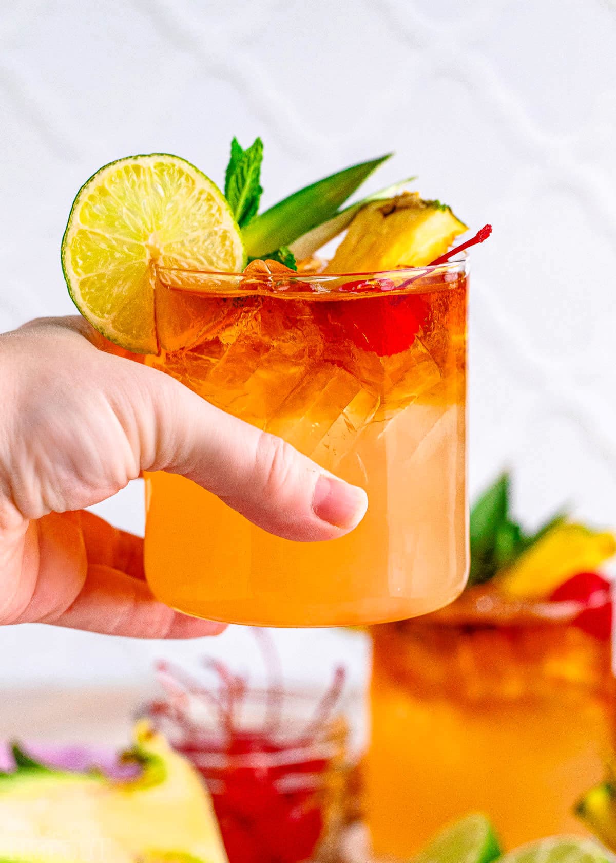 mai tai being held up above a tray and another mai tai is in the background.