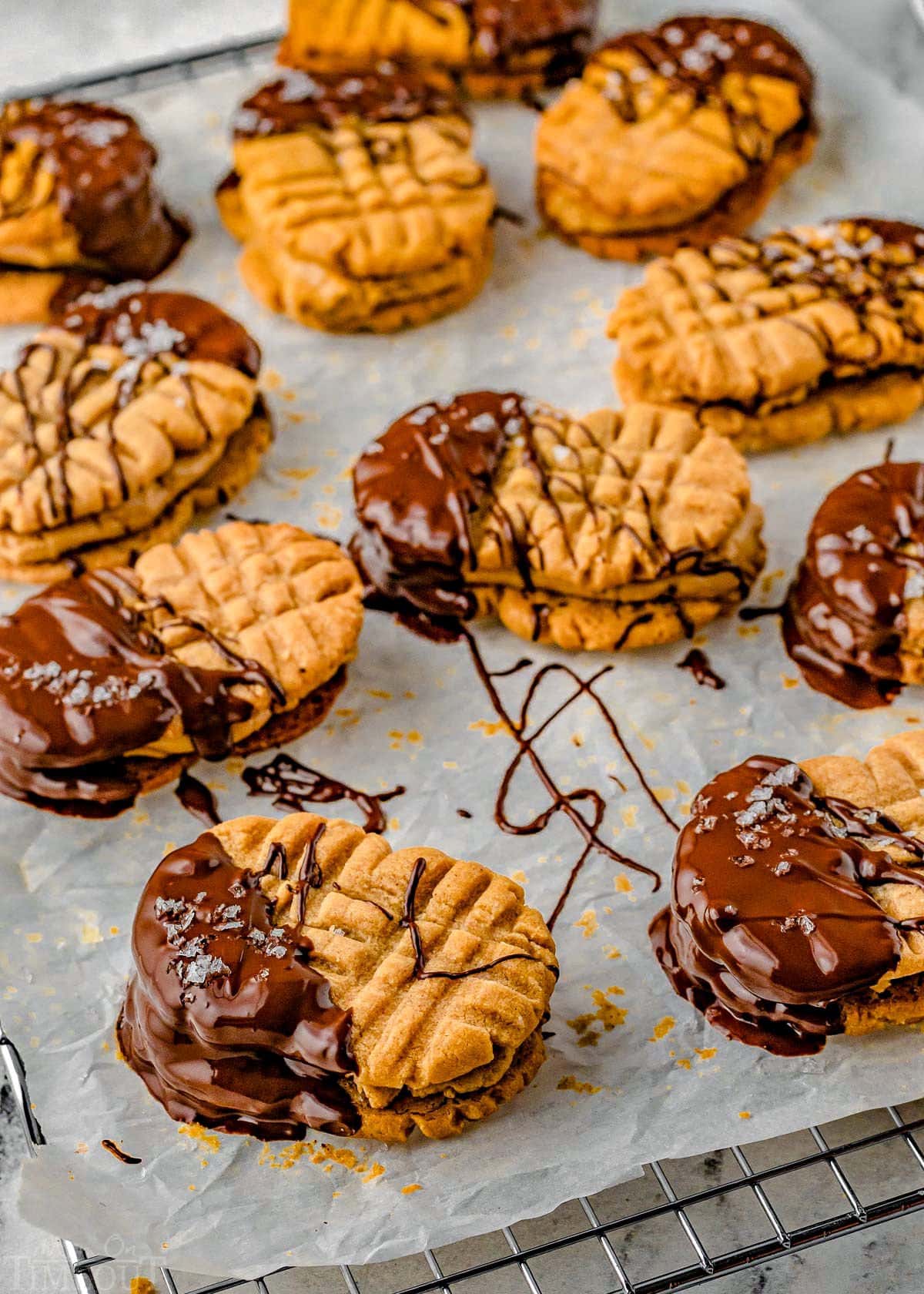 peanut butter sandwich cookies dipped in chocolate and sprinkled with flaky sea salt sitting on a parchment lined cooling rack. 