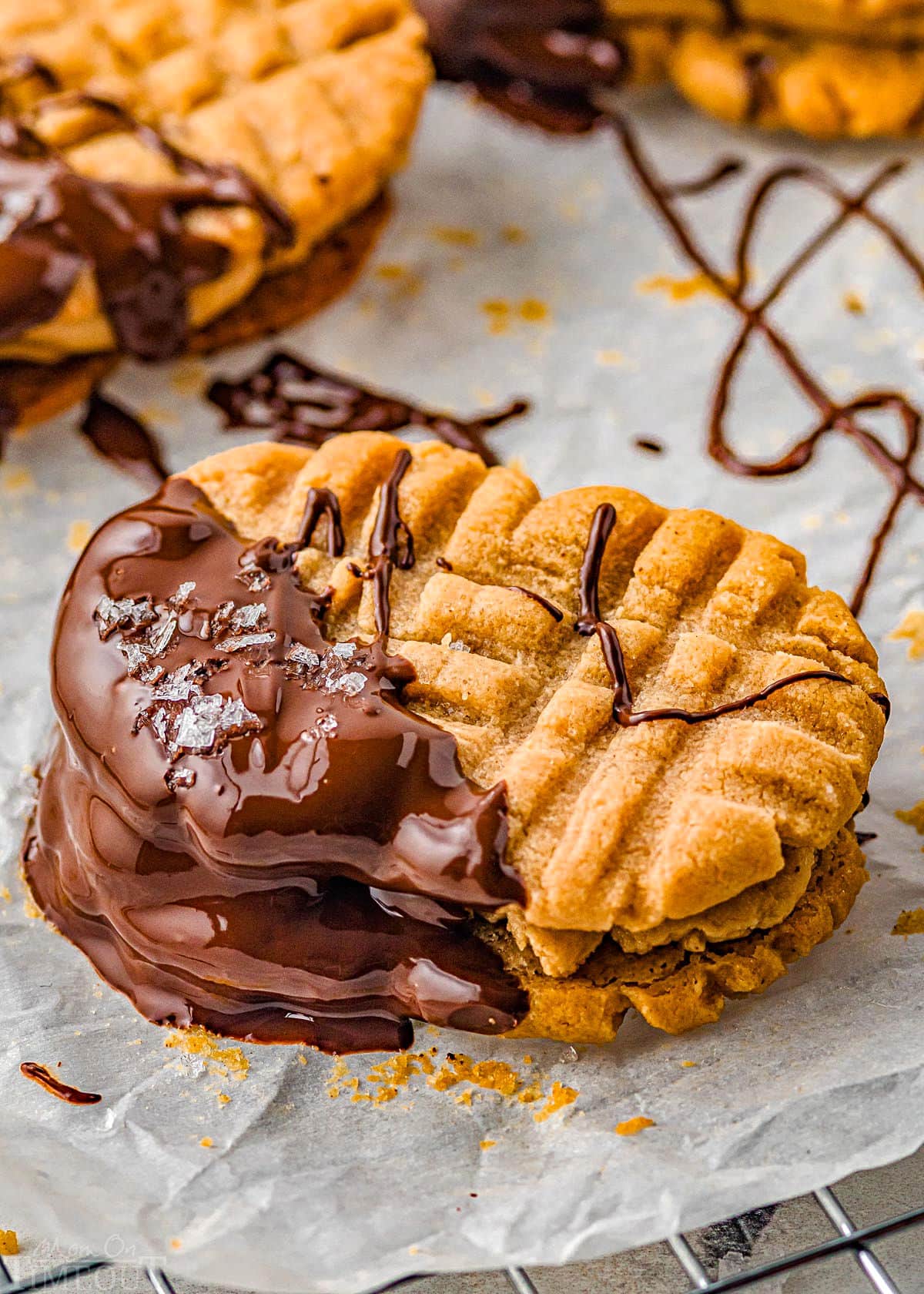 single nutter butter cookie dipping in dark chocolate and sprinkled with sea salt sitting on parchment paper while the chocolate sets up.