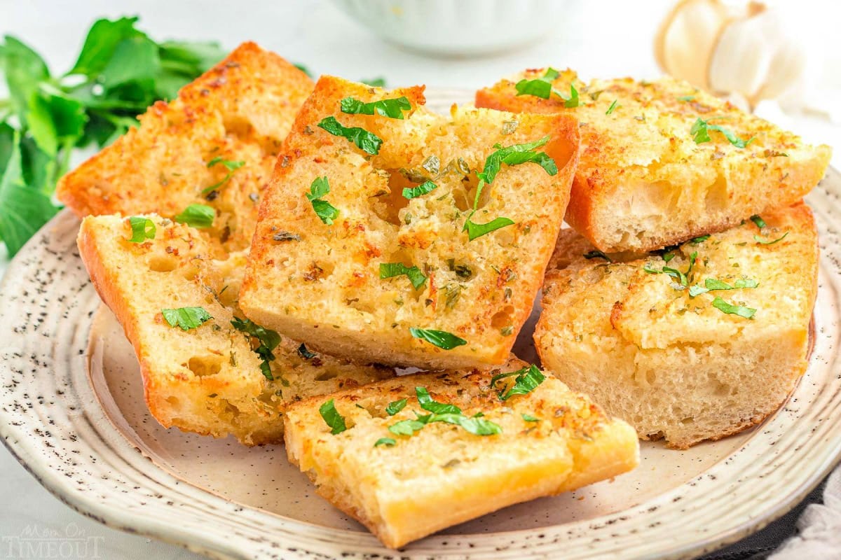 wide shot of garlic bread sliced and ready to serve off a white plate. fresh parsley garnish on the bread.