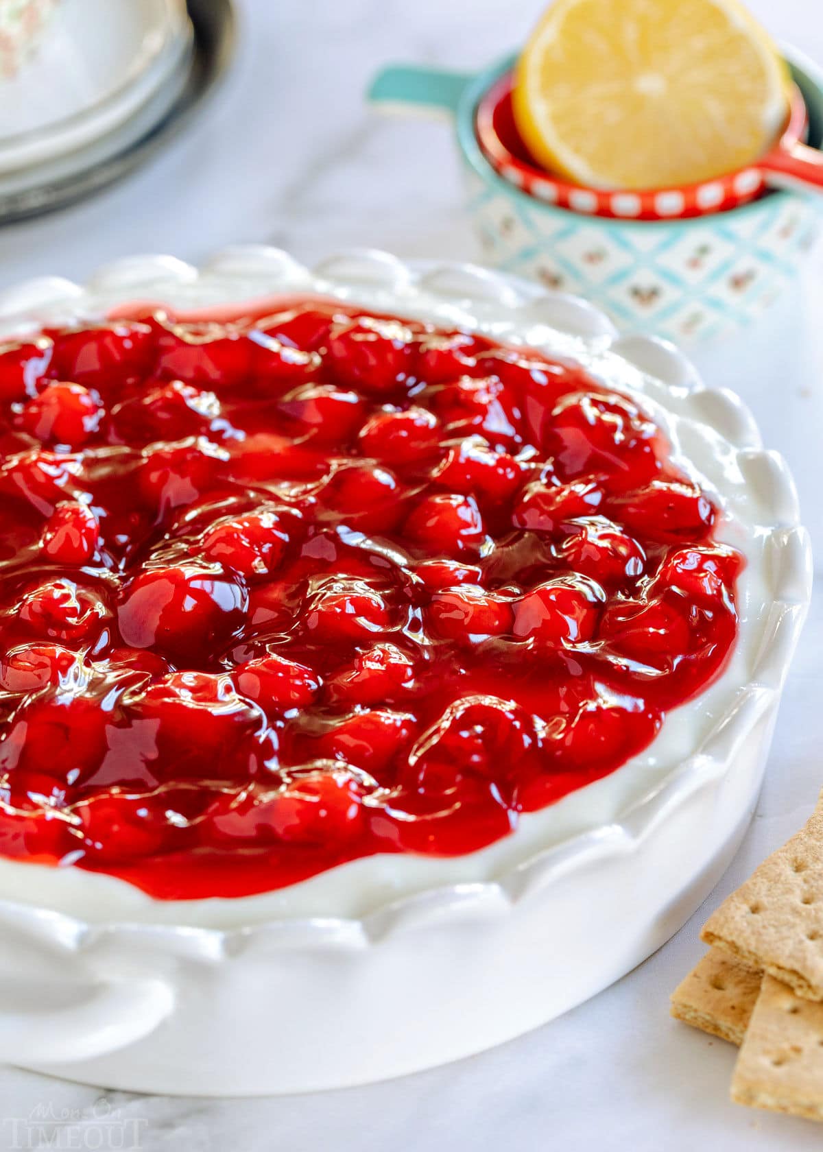 cheesecake dip topped with a can of cherry pie filling in a white scalloped pie plate.