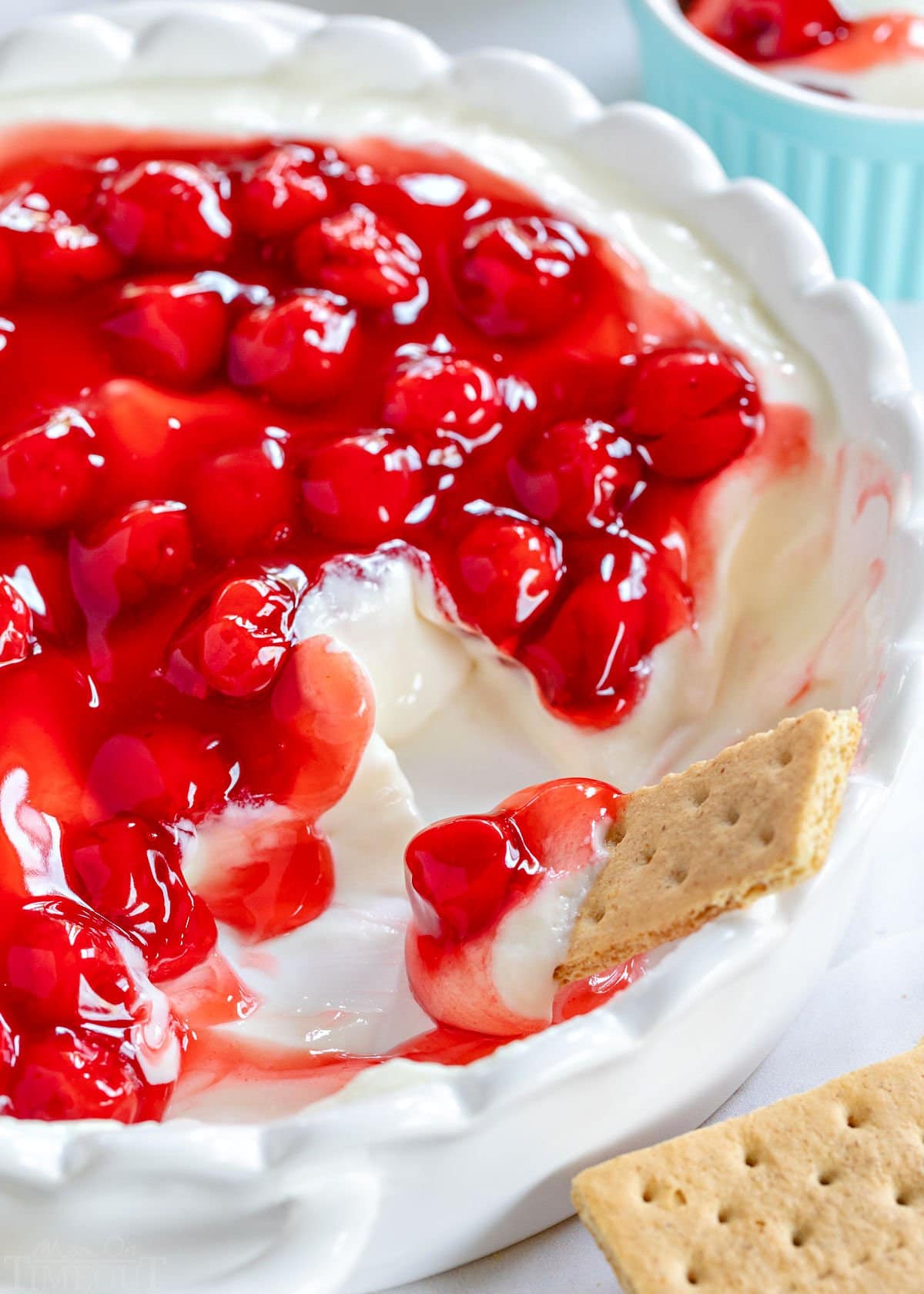 white pie plate with cherry cheesecake dip in it and a graham cracker dipping into the dip. Several servings of the dip have already been eaten.