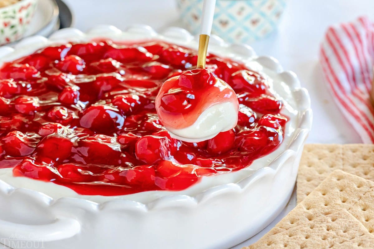 spoonful of cherry cheesecake dip held above the pie plate containing the rest of the dip.