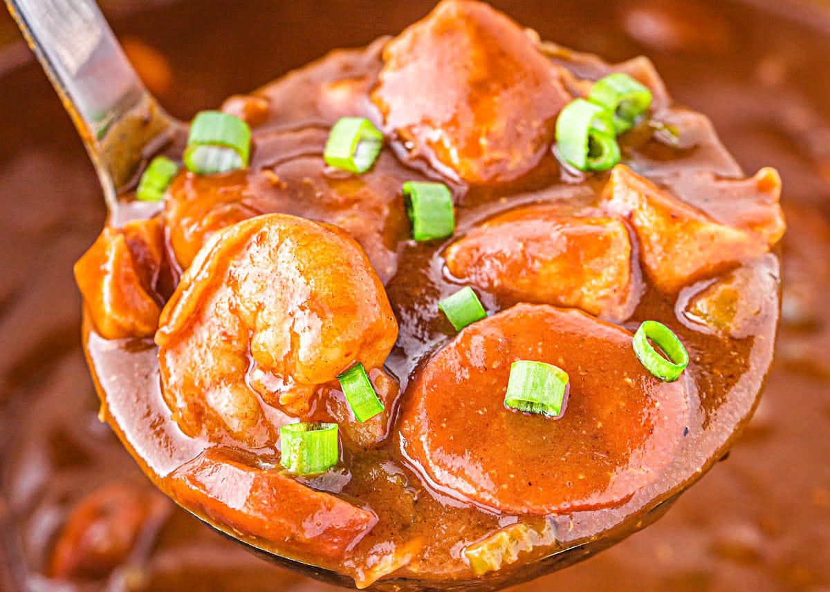 ladle full of seafood gumbo recipe garnished with a few pieces of green onion.