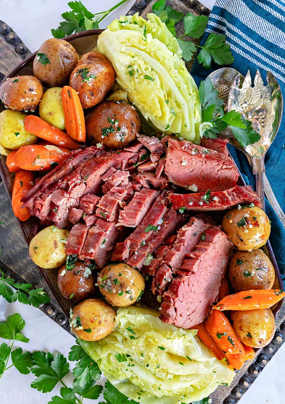 top down look at crockpot corned beef cut up with cabbage, carrots and potatoes all arranged on a serving platter ready to be served. 