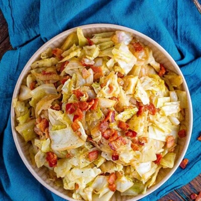 top down view of white plate filled with fried cabbage with bacon sitting on a teal napkin.