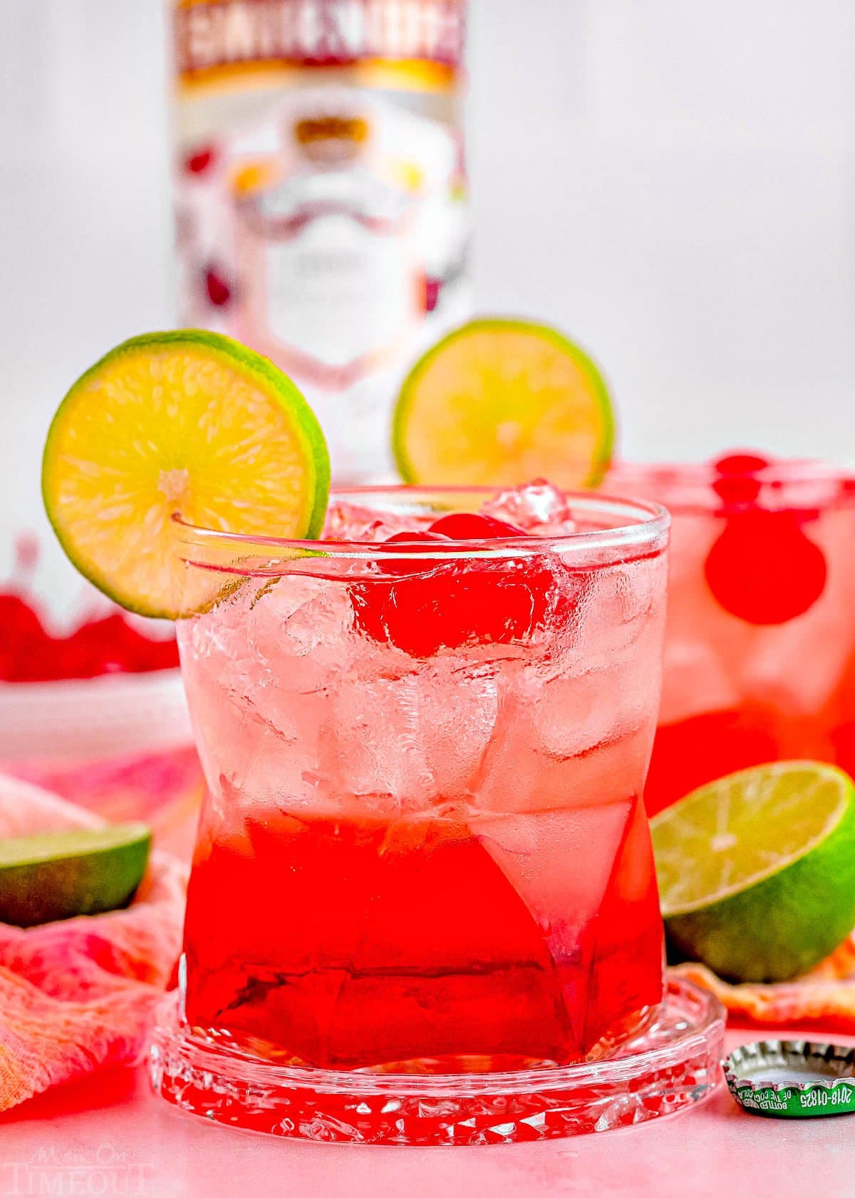 two dirty shirley temple cocktails garnished with lime and marschino cherries with the bottle of vodka in the background.