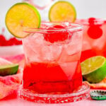 two dirty shirley temple cocktails garnished with lime and marschino cherries with the bottle of vodka in the background.