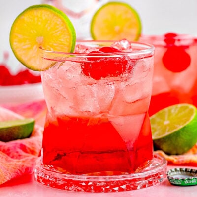 two dirty shirley temple cocktails garnished with lime and marschino cherries with the bottle of vodka in the background.