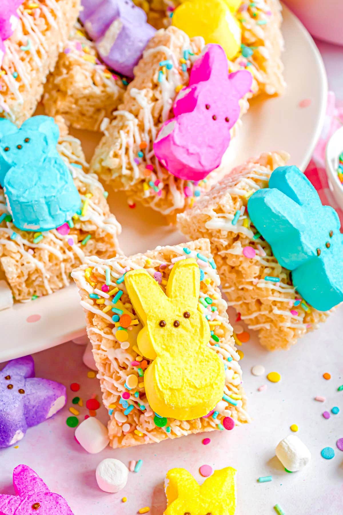 a number or rice krispie treats decorated with sprinkles and topped with an Easter peep sitting on a white plate and a few around the plate.