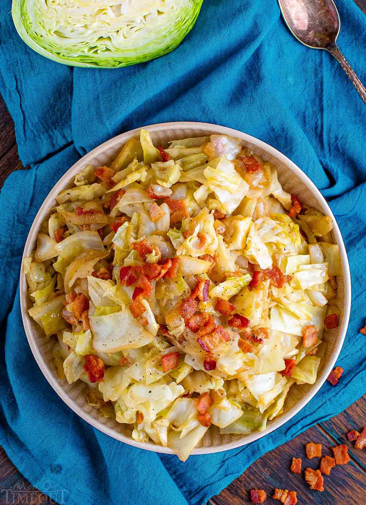 top down view of white plate filled with fried cabbage with bacon sitting on a teal napkin.