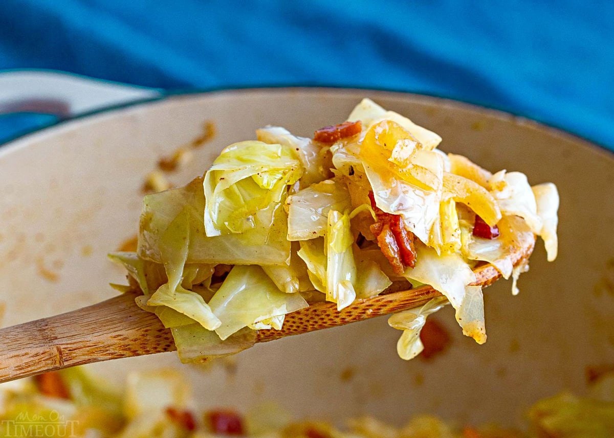 wooden spoon held over the pot of fried cabbage with a generous scoop of the fried cabbage.