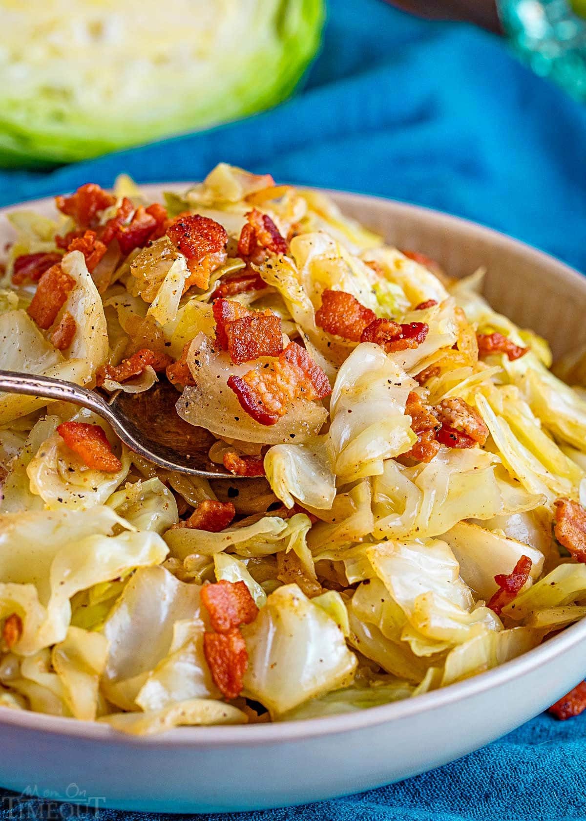 fried cabbage recipe in a white bowl with a spoon getting ready to take a bite stuck into the food.