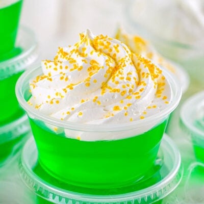 close up look at green jello shot made with vodka and topped with whipped cream and gold sanding sugar.