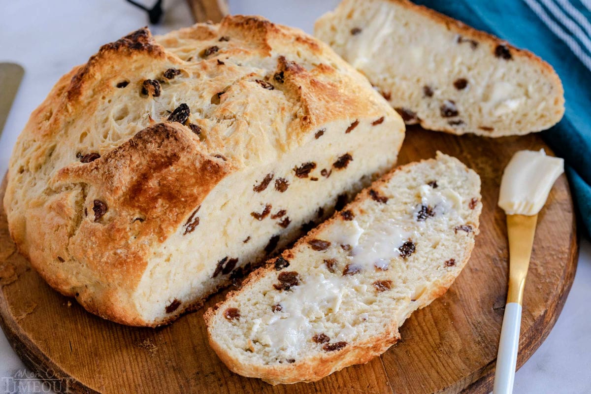 top down look at loaf of irish soda bread with one slice cut off and buttered on a round wood board.