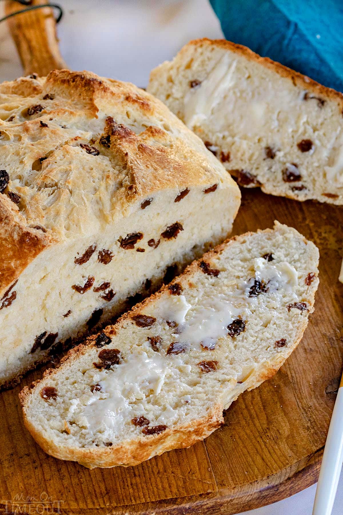 top down look at loaf of irish soda bread with one slice cut off and buttered on a round wood board.