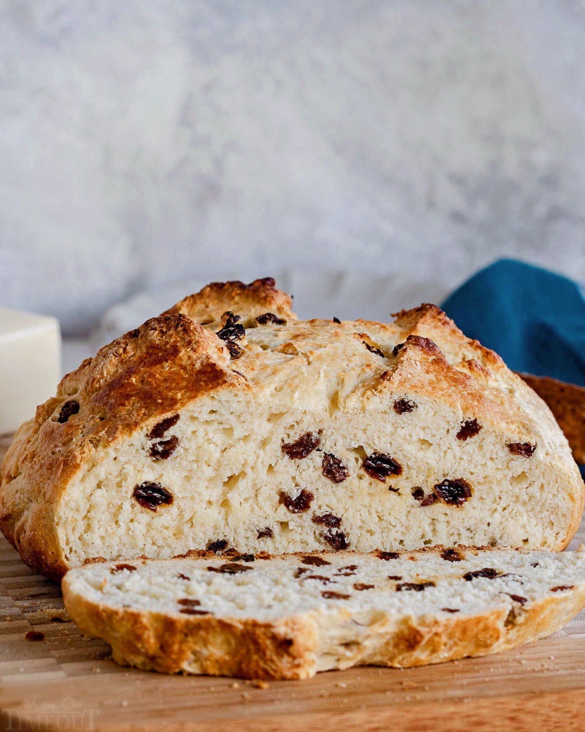 Loaf of Irish soda bread with a slice cut off and sitting on a wood cutting board with a blue napkin in the background.