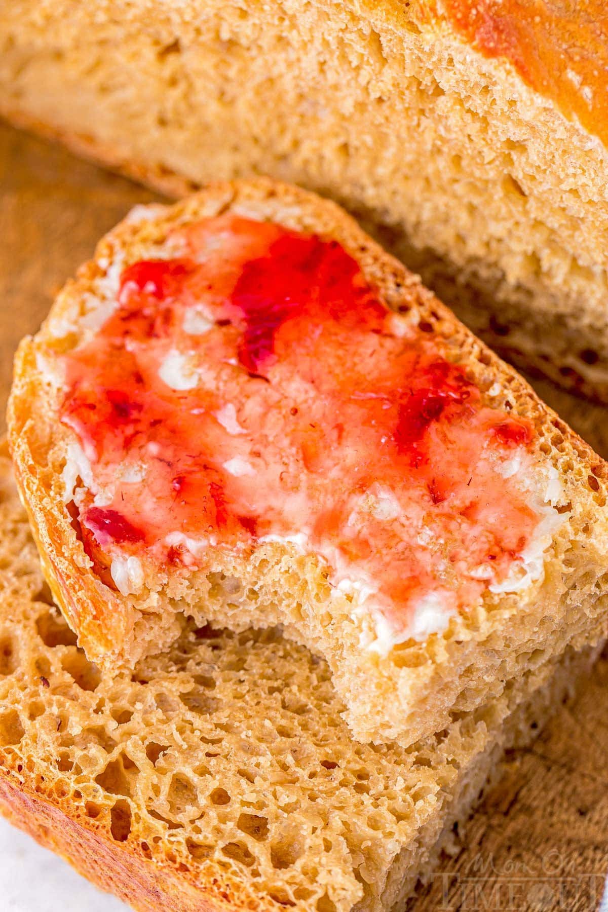 slice of bread with butter and strawberry jam sitting in front of the rest of the loaf.
