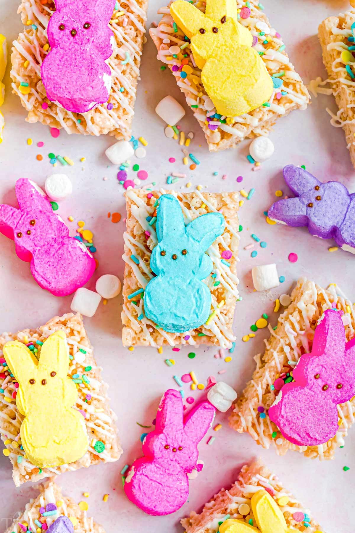 rice krispie treats decorated with white candy melts and sprinkles and topped with different colored Peeps. This is a top down view of the treats laid out on parchment paper.